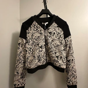 Svart och vit mönstrad bomberjacka - En snygg svart och vit tunn jacka i storlek M med ett unikt mönster. Jackan har dragkedja framtill och långa ärmar. Perfekt för höst och vår. Oanvänd. 