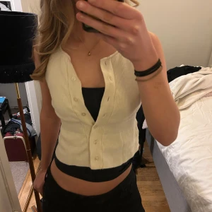 Vit ribbad västtopp - Säljer en stilren vit ribbad västtopp med knappar framtill. Perfekt för lager-på-lager eller som ett statement-plagg. Den är ärmlös och har en klassisk design som passar till många olika outfits. 💕💕