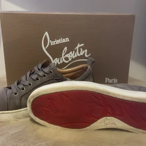  Christian Louboutin skor  - Snygga grå sneakers från Christian Louboutin i mocka med den ikoniska röda sulan. Skorna har snörning och en stilren design. Skorna är i storlek 39. Kartong och påse ingår, tyvärr har jag ej kvittot kvar. 