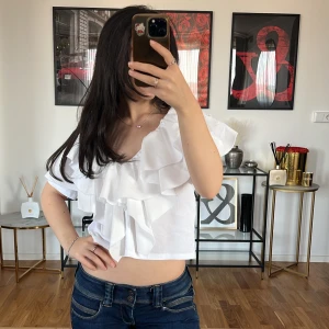 Vit volangtopp - Säljer en superfin vit topp från Zara med volanger. Den är croppad och har korta ärmar, perfekt för sommaren. Toppen är i ett lätt och luftigt material, vilket gör den idealisk för varma dagar. Den har en v-ringad design som ger en söt look💓