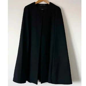 Svart lång cape från Zara - Säljer en elegant och stilren svart lång cape-kappa i ullmix från Zara. Capen har en enkel och klassisk design. Använd två gånger men i mycket bra skick. Storlek S. Köp gärna via KÖP NU 💕