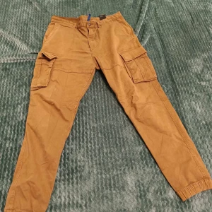 Cargobyxor - Kasta dig in i Y2K-trenden med dessa stiliga cargobyxor i desertfärg! Kombinationen av retrodesign och praktiska fickor ger både mode och funktion. Perfekta för att sätta en cool prägel på din look. Missa inte detta modefynd