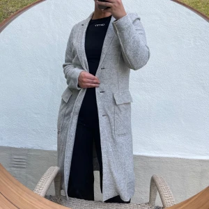Grå ullkappa - Säljer en stilren och elegant grå kappa i ull. Den har en klassisk design med knappar framtill och praktiska fickor. Perfekt för höst och vinter, stor i storleken. Passar både till vardags och festliga tillfällen.