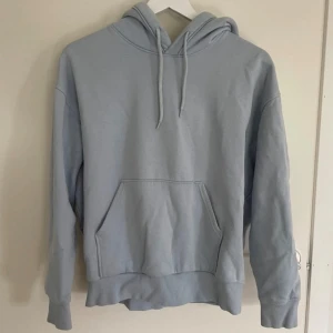 Ljusblå hoodie - Säljer en supermysig ljusblå hoodie i bra skick. Den har en klassisk känguruficka och en justerbar huva med dragsko. 