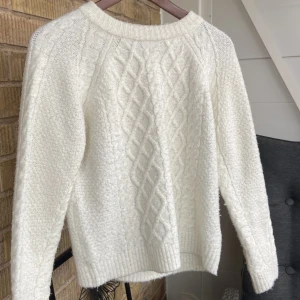 Vit stickad tröja - Mysig vit stickad tröja med ett snyggt flätmönster på framsidan. Perfekt för kyliga dagar med sin varma och bekväma passform. Tröjan har långa ärmar och ribbade kanter vid ärmslut och nederkant. Ett måste för höst- och vintergarderoben!