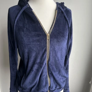 Mysig mörkblå hoodie och byxor från Majestic Filatures - Säljer en supermjuk och bekväm mörkblå hoodie med matchande byxor från Majestic Filatures. Hoodien har en dragkedja framtill och en skön huva, perfekt för mysiga dagar. Materialet är en blandning av bomull och modal, vilket gör den extra mjuk och skön att ha på sig. Perfekt för både hemmamys och avslappnade dagar ute.