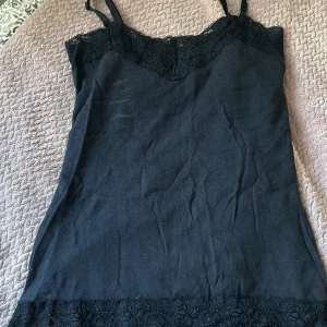 Svart linne med spetsdetaljer - Säljer ett svart linne med smala axelband som man kan justera vad för längd man vill ha. Den har en  vacker spetsdetalj både upptill och nedtill. Linnet är i bra skick. Linnet är i storlek XS och är köpt från ICHI. Linnet passar bra till allt.🫰🏻