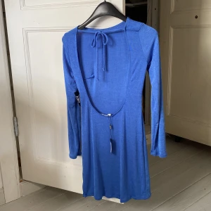 Klänning med öppen rygg  - Kort klänning med öppen rygg från Nelly. Tyget är blått med lite skimmer i. Nyskick då den aldrig är använd. 