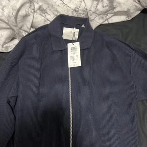 Mörkblå stickad jacka från Zara - Säljer en snygg mörkblå stickad jacka från Zara i nytt skick. Den har en dragkedja framtill och långa ärmar. Perfekt för höst och vår, med en stilren look som passar både till vardags och fest. Har aldrig använt den så lappen sitter fortfarande kvar.