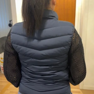 Mörkblå dunväst - Säljer en snygg mörkblå dunväst i normal passform. Västen har en dragkedja framtill och en liten logotyp på bröstet. Perfekt för höst och vår när du vill hålla dig varm men ändå se stilren ut. Passar både till vardags och lite mer avslappnade tillfällen.