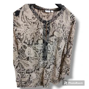 Snygg Blus i Nyskick  - Festlig Blus i nyskick. I färgerna beige och svart. Genomskinlig.  Fint med ett svart linne under.   OBS: Bilderna är tagna av mig. 2Xl