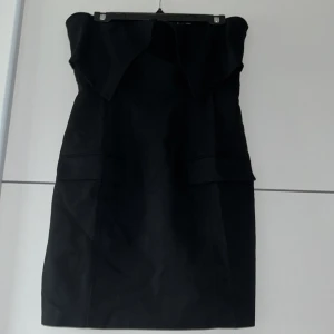 Svart axelbandslös klänning från ADOORE - Snygg svart axelbandslös klänning från ADOORE i en elegant och stilren design. Perfekt för festliga tillfällen. Klänningen har en tight passform och en dragkedja bak för enkel påklädning. Den är tillverkad i ett mjukt och bekvämt material som ger en smickrande siluett. Men är liten i storleken så den passar 38. Jätte snygg till nyårsfirande, kan mötas upp om det är nära Malmö 