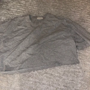 Grå croppad t-shirt från Gina Tricot - Säljer en enkel och stilren grå croppad t-shirt från Gina Tricot. Perfekt för en avslappnad look. T-shirten är i ett mjukt material och har en normal passform. Passar bra till både jeans och kjol!