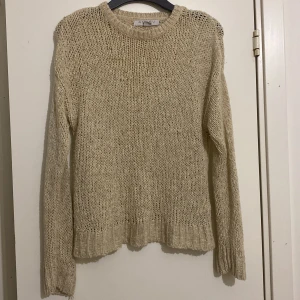 Beige stickad tröja - Mysig beige stickad tröja i mycket bra skick. Perfekt för höst och vinter med sin varma och bekväma design. Man kan se igeom tröjan då den är stickad så perfekt flr fest, den är beige guld aktig och har glitter i sig 