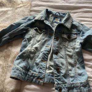 Ljusblå jeansjacka från Lee - Säljer en snygg ljusblå jeansjacka från LOGG. Jackan har klassiska bröstfickor med knappar och en stilren design. Perfekt för vår och sommar! Stl 152
