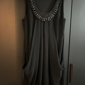Svart klänning med pärldetaljer - Snygg svart klänning med en fantastisk pärldetalj runt halsringningen. Perfekt för en festlig kväll! Klänningen är ärmlös och har en lös passform som ger en elegant och bekväm känsla. Materialet känns mjukt och faller fint.