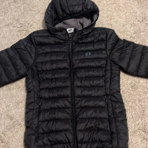 Svart pufferjacka från Hang Ten - Säljer en svart pufferjacka från Hang Ten i storlek XS. Jackan har en dragkedja framtill och en mysig huva. Perfekt för kyliga dagar och håller dig varm och bekväm. Den är i mycket bra skick och redo för nya äventyr!