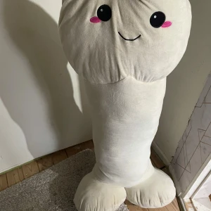 Snopp kudde  - En stor, beige plyschkudde formad som en söt figur med ett leende ansikte och rosa kinder. Kudden är mjuk och perfekt för att krama eller använda som en rolig inredningsdetalj. Den har en unik form som gör den både rolig och mysig att ha i rummet.