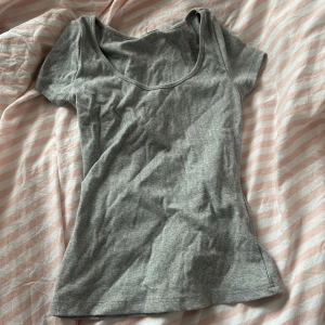 Grå ribbad topp - Säljer en enkel och stilren grå ribbad topp med korta ärmar. Perfekt för vardagsbruk eller som basplagg. Toppen har en rundad halsringning och är i ett mjukt och bekvämt material. Säljer pga den inte kommer till användning <3