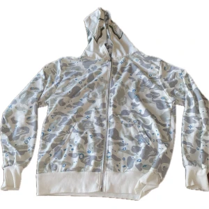 En fin Hoodie som använts fåtal gånger och är i bra skick! - Säljer en cool vit och grå camo hoodie med hajmotiv på huvan. Den har en dragkedja framtill och är i mycket bra skick.