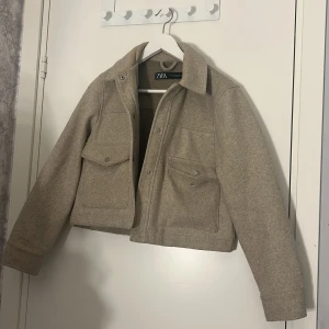 Beige jacka från Zara - Säljer en snygg beige jacka från Zara i storlek XS. Jackan är croppad och har en stilren design med knappar framtill och två stora fickor på bröstet. Perfekt för höst och vår när du vill ha något lätt men ändå stiligt. 🧥✨