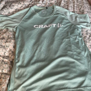 Ljusgrön t-shirt från Craft - Säljer en ljusgrön t-shirt från Craft i storlek M. Perfekt för träning med sitt lätta och bekväma material. T-shirten har korta ärmar och en rund halsringning. Den är i nyskick och redo för nya äventyr! Pris kan diskuteras.