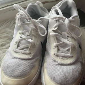 Vita Nike sneakers - Säljer ett par vita Nike sneakers i storlek  40. De är i bra skick med klassisk snörning och en svart Nike-logga på sidan. Perfekta för vardagsbruk eller träning. Skorna har en bekväm passform och är gjorda i syntetmaterial.