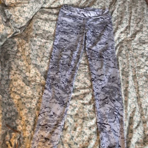 Grå camo leggings från PX5 - Säljer ett par grå camo leggings från PX5. De är gjorda i ett stretchigt material av 92% polyester och 8% elastan, perfekt för träning eller vardagsbruk. Mönstret är i olika nyanser av grått och svart, vilket ger en cool look.