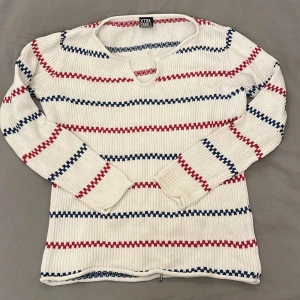 Vit randig tröja från Xtra Small - Säljer en vit ribbad tröja från Xtra Small med röda och blå ränder. Tröjan har en v-ringad hals och långa ärmar. Perfekt för en avslappnad stil. Jätte gullig ute i skärgården på sommaren!☀️☀️