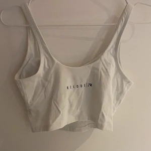 Vit linnetopp från Relode - Snygg vit linnetopp från Relode med breda axelband och en enkel design. Perfekt för träning eller en avslappnad dag. Toppen har en diskret logga framtill.