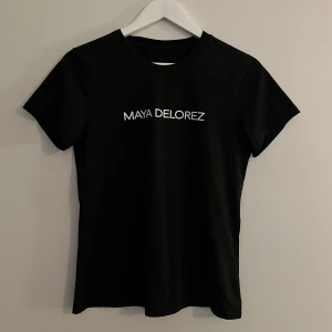 Svart t-shirt från Maya Delorez - Snygg svart t-shirt från Maya Delorez med vit logga på bröstet. 