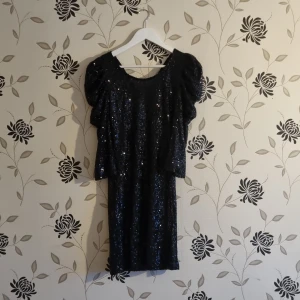 Svart Paljettklänning trån "Just Female", Strl: XS/34, - Snygg svart klänning med glittriga paljetter och korta ärmar. Perfekt för en festlig kväll. Klänningen har en dragkedja i ryggen och en figurnära passform. Märke, Just Female från Danmark. Testad men ej använd - fint skick!