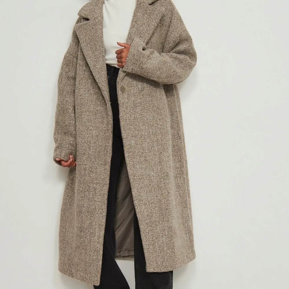 Snygg och stilren beige kappa med lång passform och klassisk krage. Perfekt för kyligare dagar med sin mjuka och bekväma design. Den här kappan är något oversized och gjord av ull och har en krage med slag, en knappstängning på framsidan, långa ärmar, snedställda sidofickor. Aldrig använd, blivit lite skrynklig för den legat i en låda. Bilder finns :) . Takit.