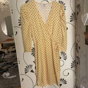 Beige omlottklänning med prickar från Bubbleroom - Säljer en beige omlottklänning från Monki med svarta prickar. Klänningen har långa ärmar och knytband i midjan för en smickrande passform. Perfekt för både vardag och fest!