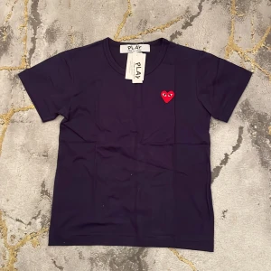 Svart t-shirt från Comme des Garçons - Snygg svart t-shirt från Comme des Garçons med det ikoniska röda hjärtat på bröstet. Perfekt för en stilren look. Storleken är S men egentligen typ som XS. 