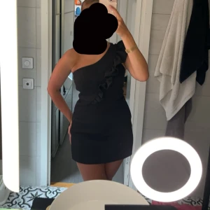 Svart oneshoulder klänning - Elegant svart oneshoulder jumpsuit, dock ser de ut som en klänning, med volangdetalj längs axeln.. Storlek S och har enbart används en gång. Nypris 700kr 