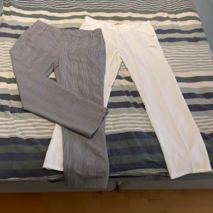 Två par byxor i olika stilar - Säljer två par byxor. Ett par är vita med en rak passform och diskreta detaljer. Det andra paret är grått med ett randigt mönster och en mer formell look. Perfekta för olika tillfällen och stilar. Buda på går att köpa styckvis.