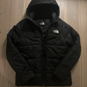Svart vinterjacka från North Face  - Säljer den här supersnygga dunjackan från North Face, i stolek S. Jackan är i mycket bra skick då den bara blivit använd fåtal gånger, däremot ett pyttelitet håll på framsidan av jacka (kolla bilder) men inget man ser vid användning. Finns resorband på insidan så man kan dra ihop jackan till en mer smickrande form. Perfekt nu till vintern med luva och sin pufferdesign för att hålla värme! Säljer för att den inte kommer till användning längre. 