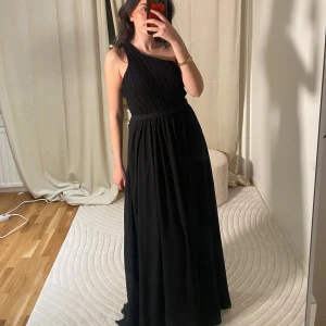 Svart balklänning  - Elegant svart långklänning med oneshoulder-design och vackert spetsmönster på ryggen. Perfekt för balen, bröllop o högtider. Strl M men passar mig som bär S. Köpt i spanien för ett år sen, och i super bra skick!