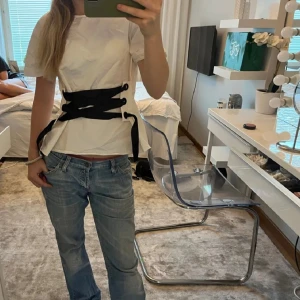 Vit t-shirt med svart snörning - Trendig vit t-shirt med unik svart snörning framtill. Perfekt för att ge en edgy touch till din outfit. Kortärmad och i en bekväm passform. Priset kan diskuteras, använd 1 gång 