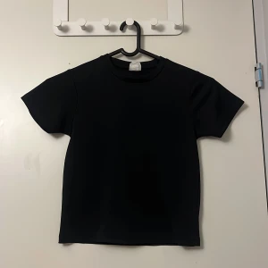 Svart t-shirt från Eskilstuna Gymnastikförening - Snygg svart t-shirt med Eskilstuna Gymnastikförenings logga i vitt på baksidan. Perfekt för träning eller vardagsbruk. Kortärmad och tillverkad i mjukt material för extra komfort. Storleken är oklar men skulle säga kanske 128 eller 134.