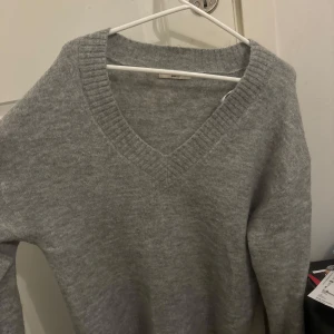 Grå stickad tröja från Gina Tricot - Mysig grå stickad tröja från Gina Tricot med v-ringning. Perfekt för kyliga dagar och enkel att matcha med olika outfits. Knappt använd och oversize i storlek