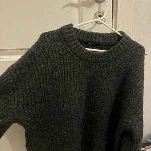 Mörkgrå stickad tröja från Gina Tricot - Säljer en mysig mörkgrå stickad tröja från Gina Tricot. Tröjan har en ribbad design med långa ärmar med slits på armarna och sidorna