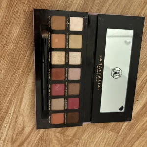 Ögonskuggspalett från Anastasia Beverly Hills - Snygg ögonskuggspalett med 14 olika nyanser från Anastasia Beverly Hills. Paletten innehåller både matta och skimrande färger, perfekt för att skapa varierande looks. Inbyggd spegel och dubbeländad borste ingår. Endast använt en gång bara sedan bara legat kvar i byrån 