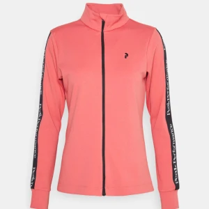Peach tröja från Peak Performance - Snygg peach tröja från Peak Performance med dragkedja framtill och logotyp längs ärmarna. Perfekt för en sportig look. Jackan har en hög krage och långa ärmar. Finns en ficka med dragkedja vid höften. Ny med prislapp, nypris 1399kr