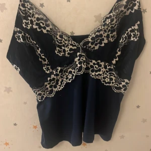 Mörkblå linne med spetsdetaljer - Elegant mörkblå linne med vackra spetsdetaljer i vitt. Linnet har smala axelband och en feminin design som passar perfekt för en stilren look.