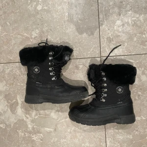 Svarta vinterboots  - Höga vinterboots med vadderat skaft i nylon. Vattentätt membran som andas. Varmt foder i fuskpäls och fleece. 
