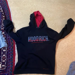 Svart hoodie från Hoodrich - Säljer en svart hoodie från Hoodrich med röd insida i huvan och tryck på både fram- och baksida. Perfekt för en avslappnad stil.