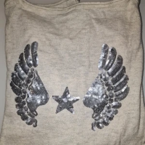 Tröja med vingar - Säljer en mysig tröja från Caddis Fly med silverfärgade paljetter i form av vingar och en stjärna på ryggen. Perfekt för att ge lite extra bling till vardagslooken!