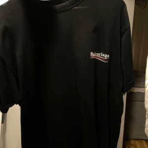Svart t-shirt från Balenciaga - Snygg svart t-shirt från Balenciaga med logotyp i vitt och rött på bröstet och ryggen. Perfekt för en stilren look. Cond 9/10. Knappt använd, handtvättad. Priset går att diskutera. Size s, passar M. Finns inte ofta denna modell ute.. 